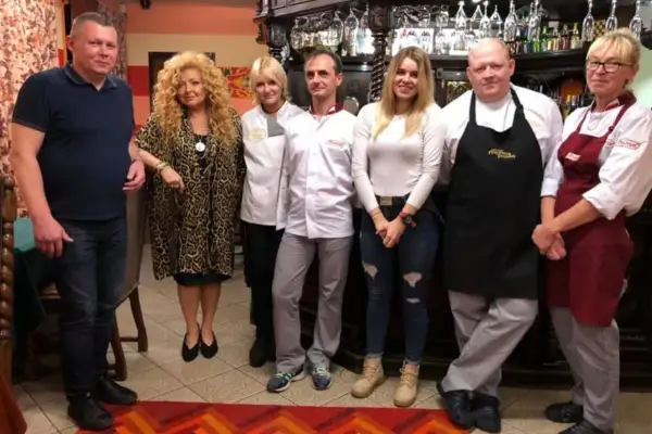 Grupa osób pozuje do zdjęcia w restauracji. Wszyscy wyglądają na zadowolonych, jakby mieli zamiar przyjemnie podjadać.